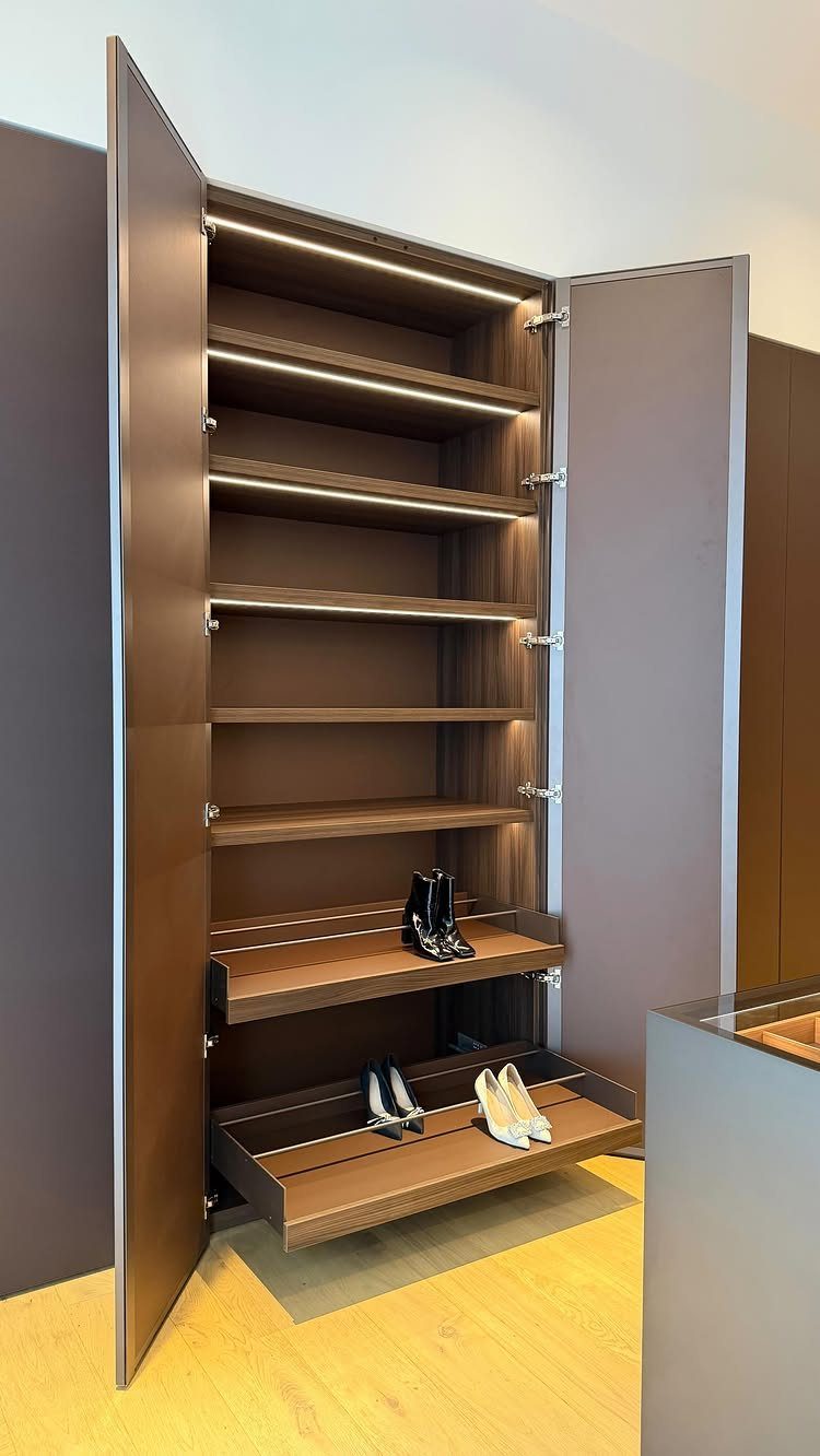 Open brown wooden closet with integrated lighting and pull-out shoe drawers.