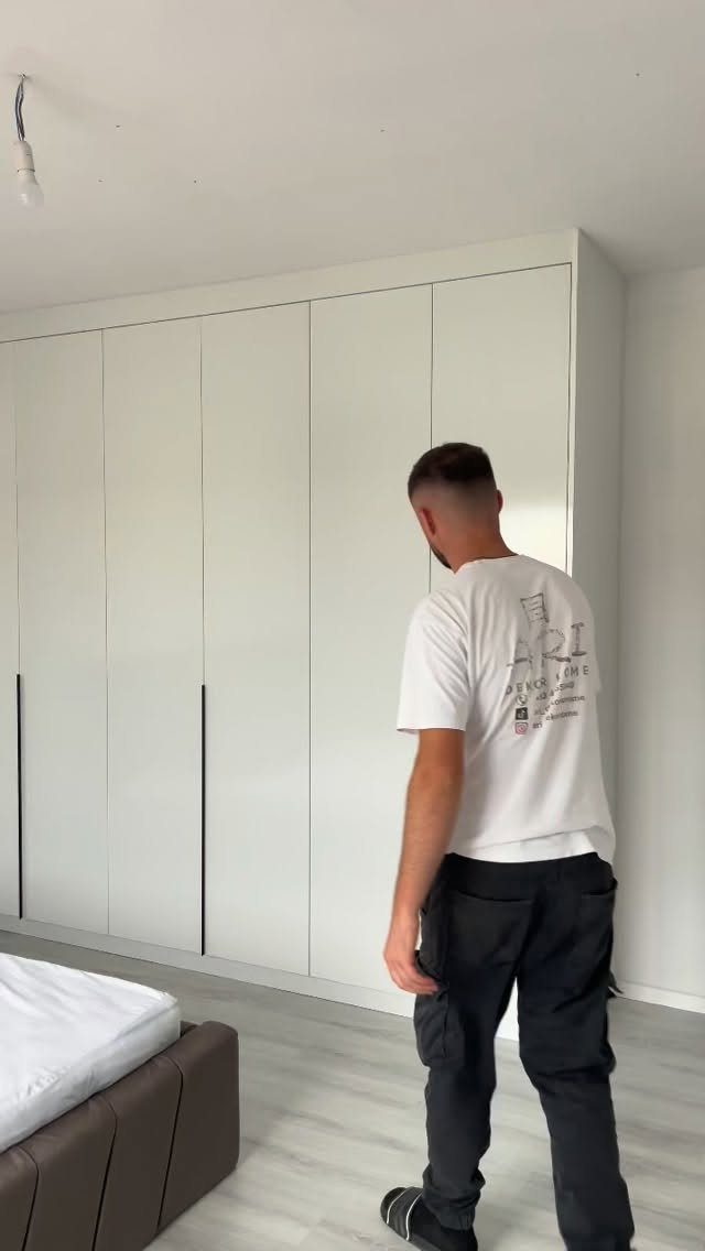 Man standing next to a large white built-in closet in a modern bedroom