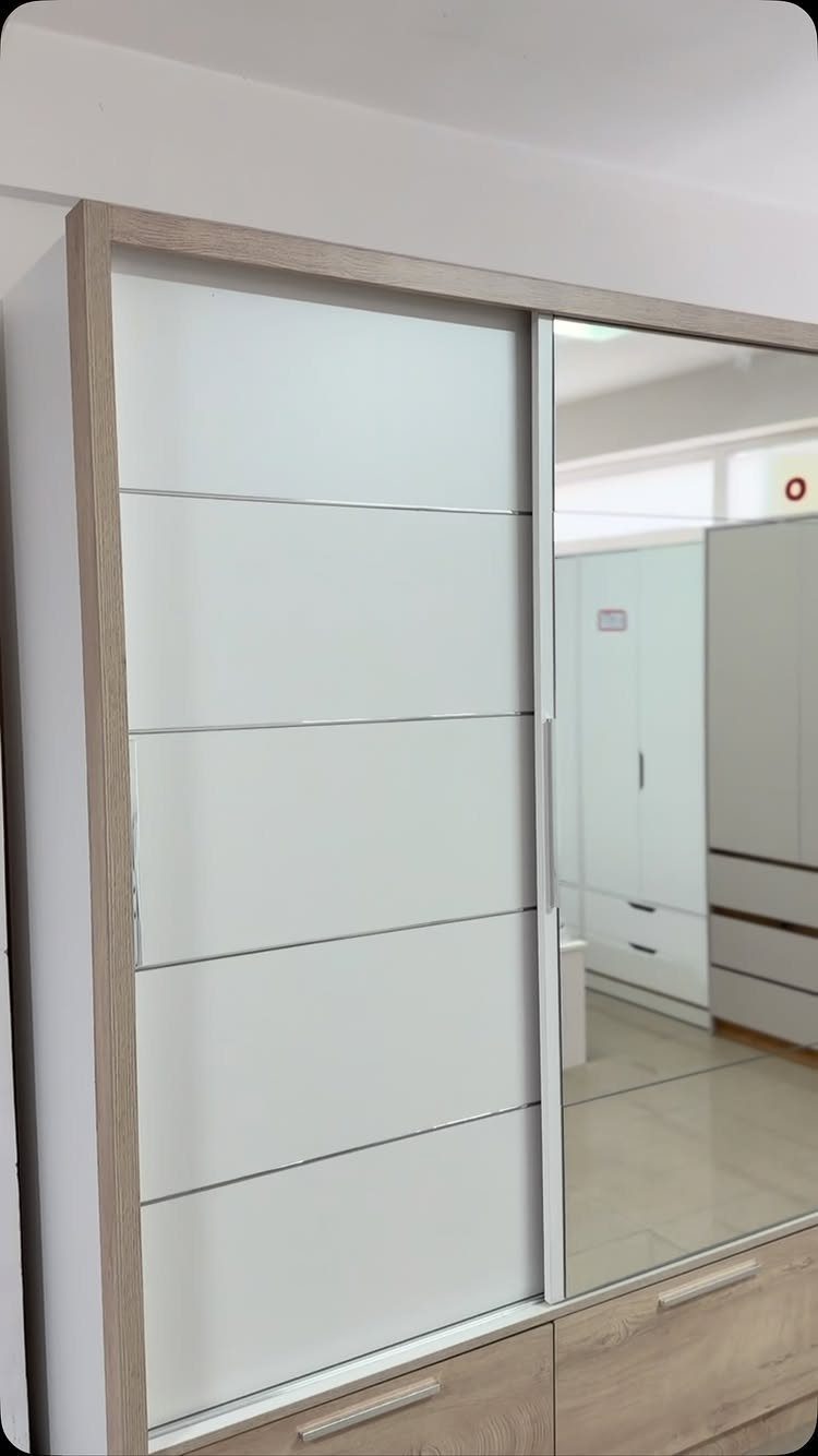 Modern white wardrobe with sliding paneled and mirrored doors in a bright room