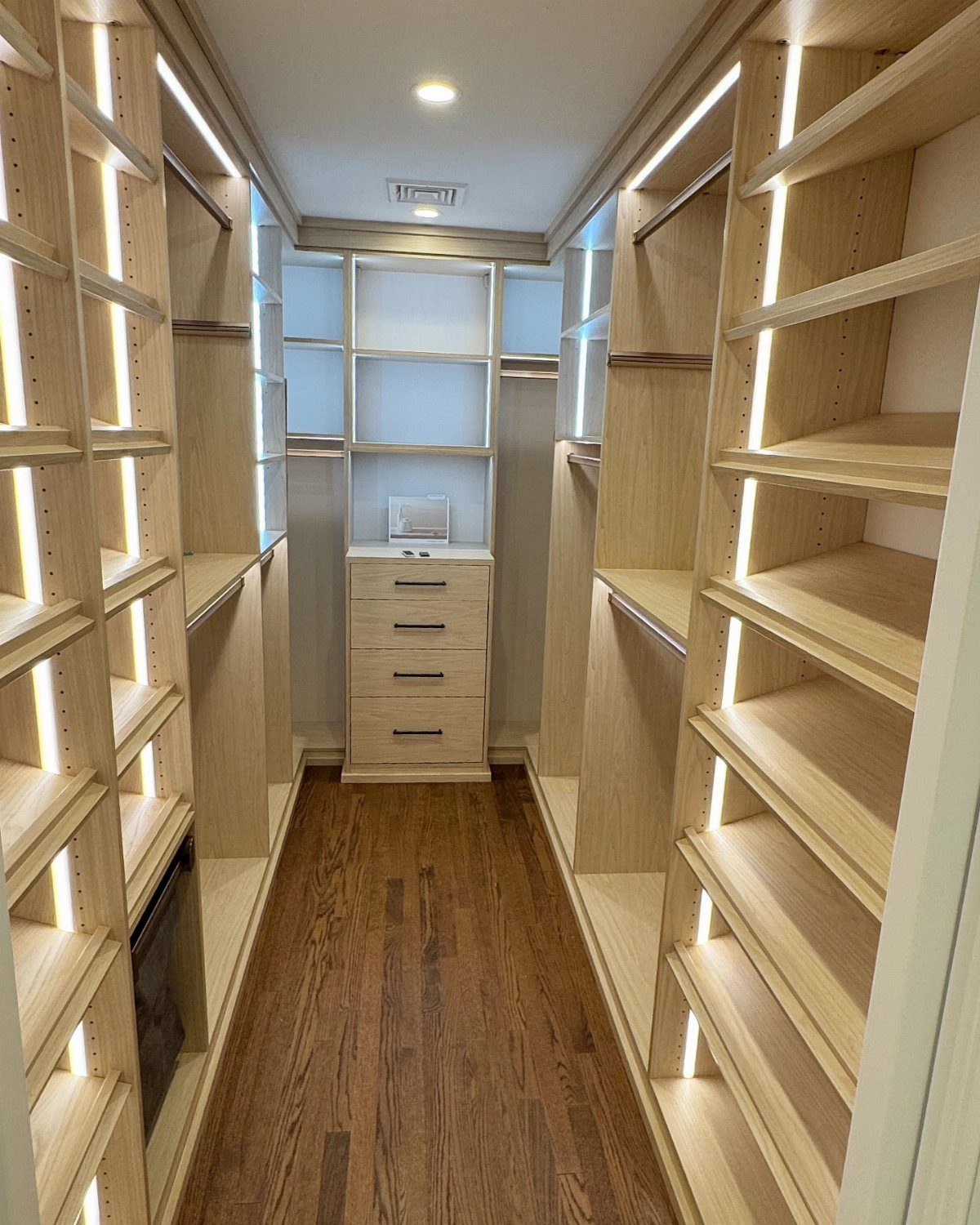 Walk-in closet with light wood shelving and integrated vertical LED strip lighting.
