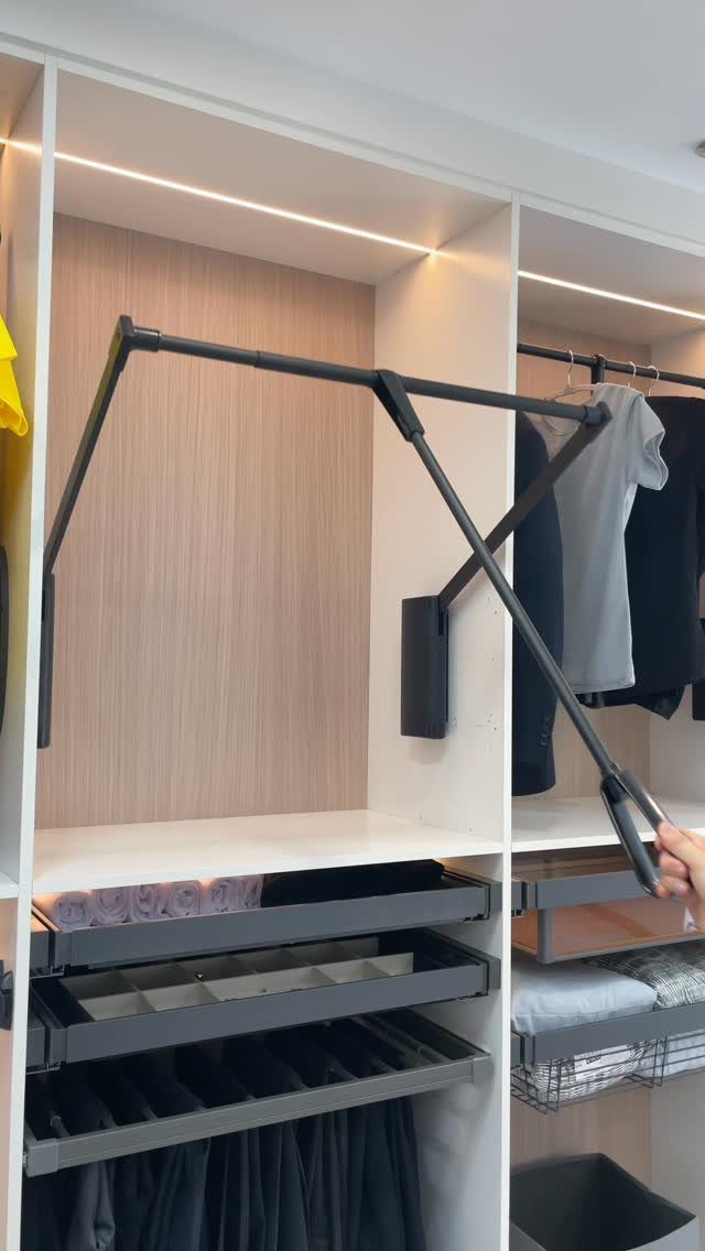 Pull-down wardrobe rod being lowered in a modern white and wood-grain closet system.