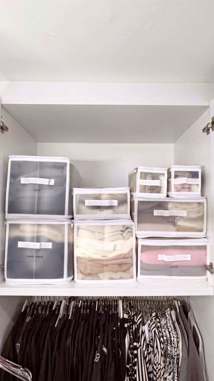 Clear plastic storage bins with folded clothes stacked on a white closet shelf.