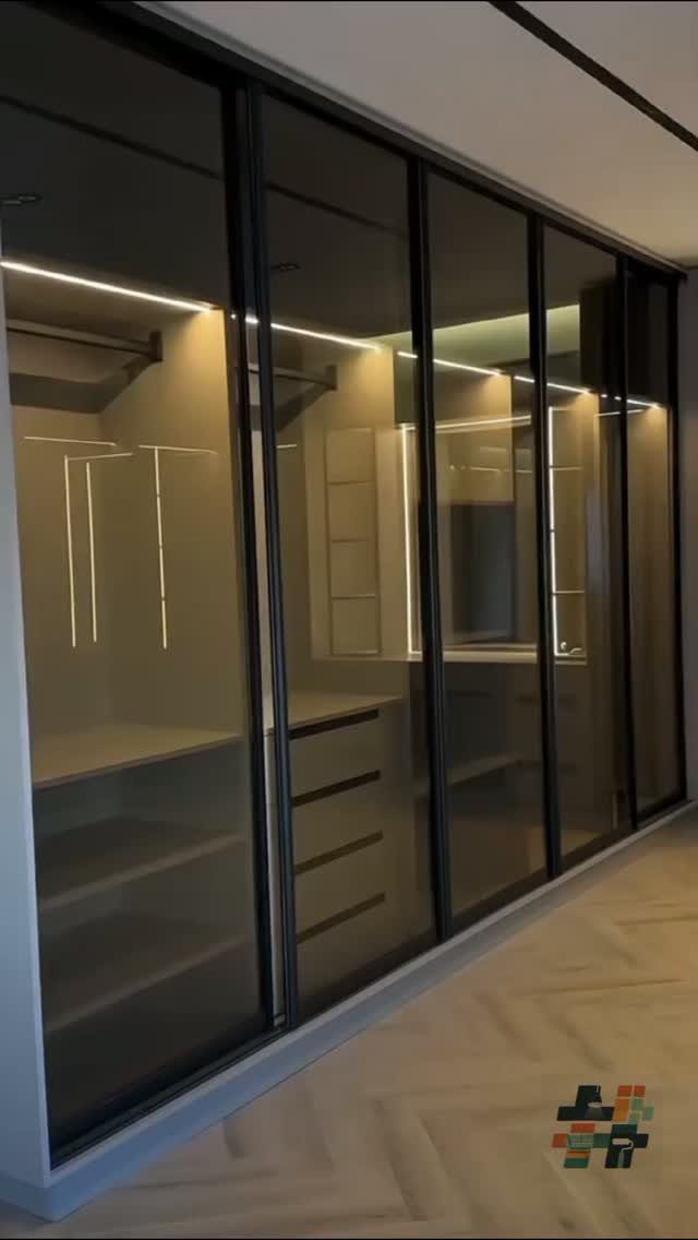 Modern walk-in closet with glass sliding doors, integrated lighting, and custom shelving units.