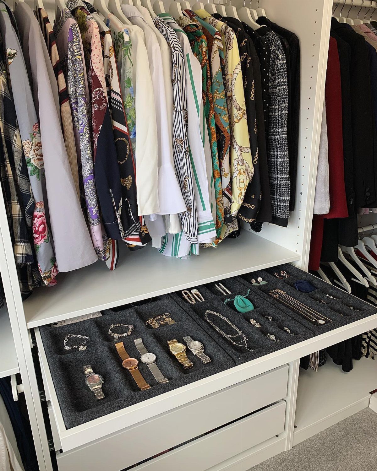 White walk-in closet with hanging clothes and an open jewelry organizer drawer.