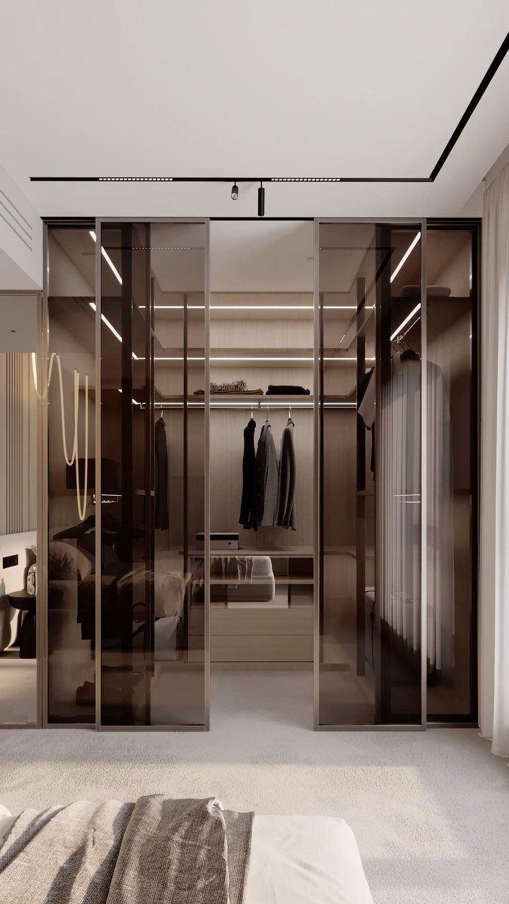 Tinted glass sliding doors opening into a modern, illuminated walk-in closet with clothing.