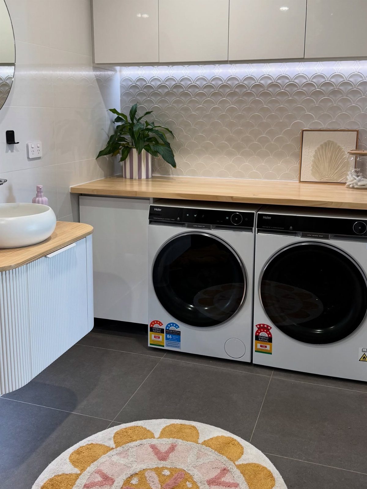 Two white front-load laundry machines under a wooden counter in a modern laundry room.