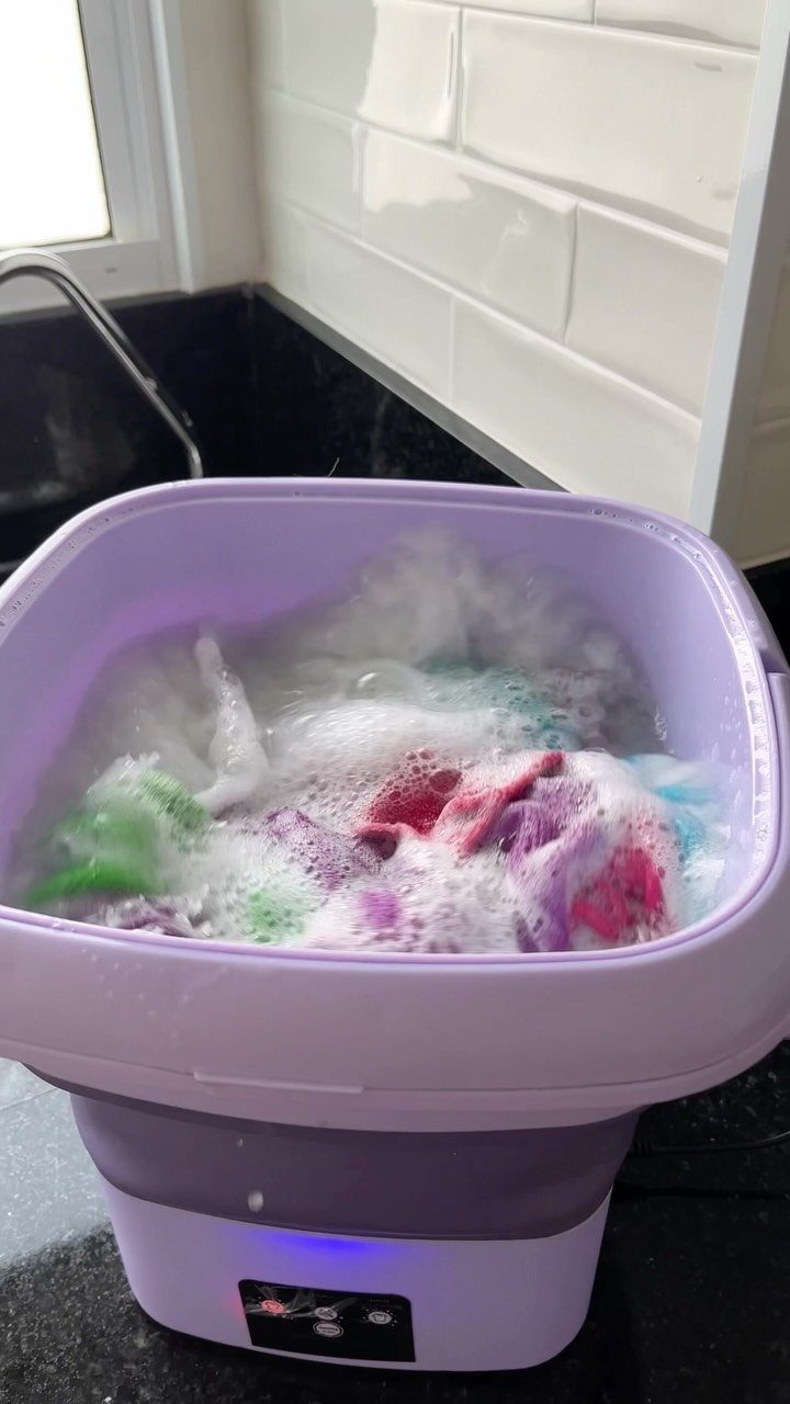 Purple portable washing machine with soapy clothes on a black kitchen countertop.