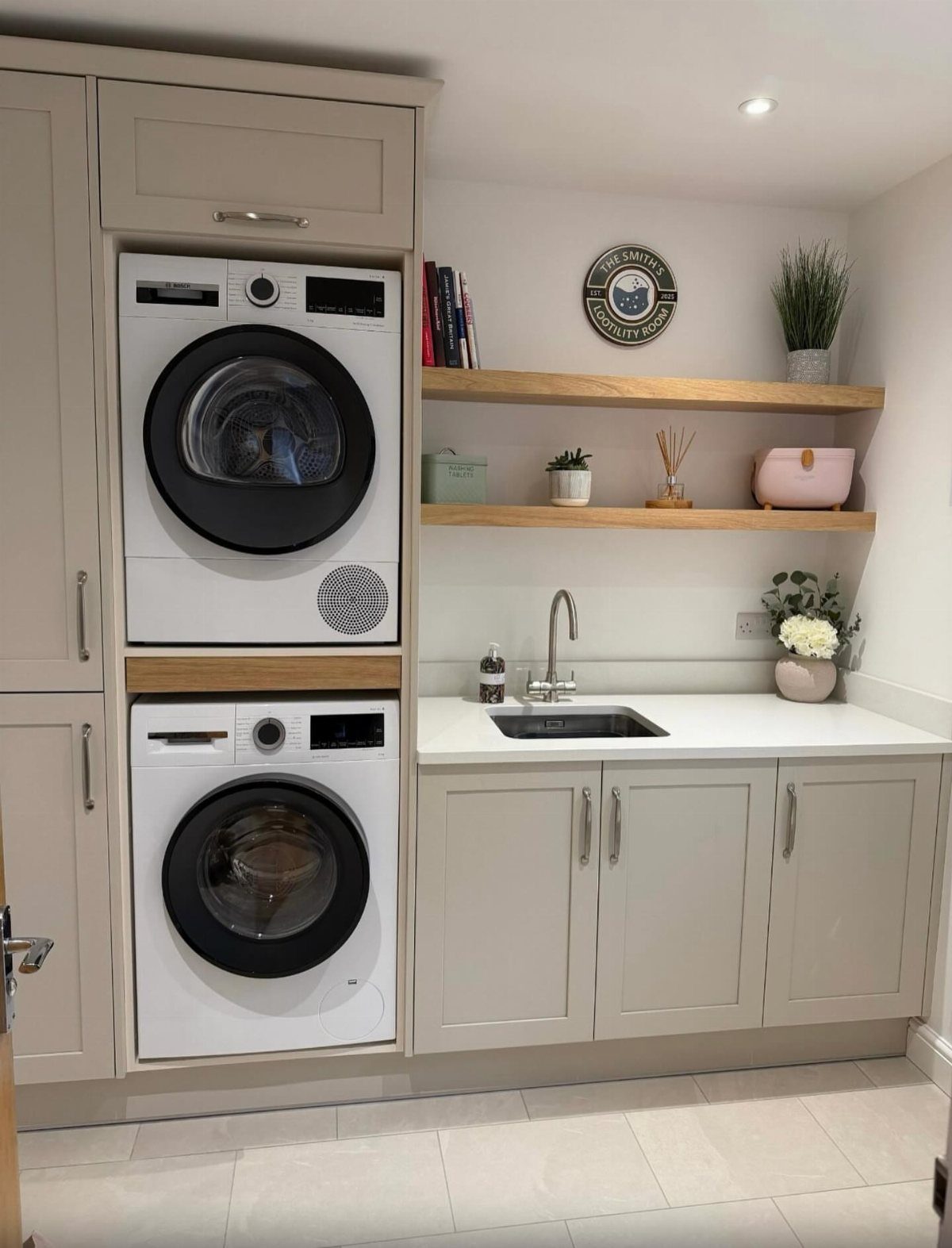 Stacked white washer and dryer integrated into grey cabinetry next to a sink.