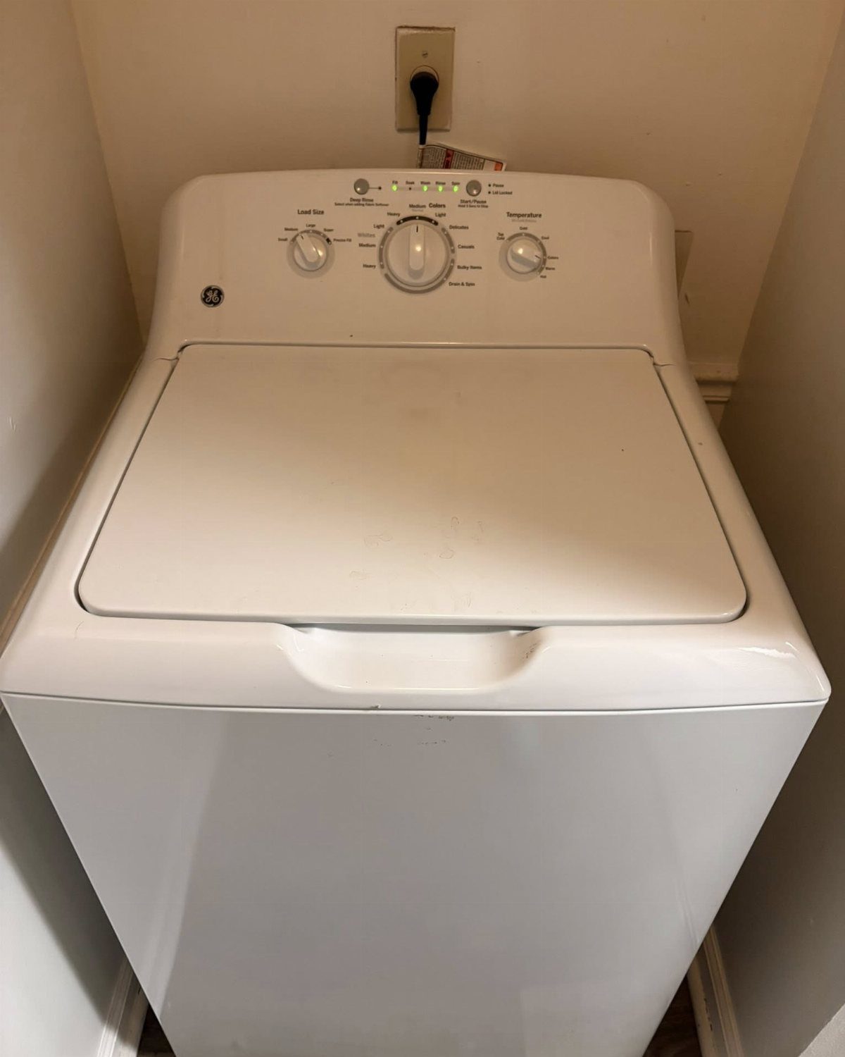 White top-loading washing machine installed in a narrow white apartment laundry closet.