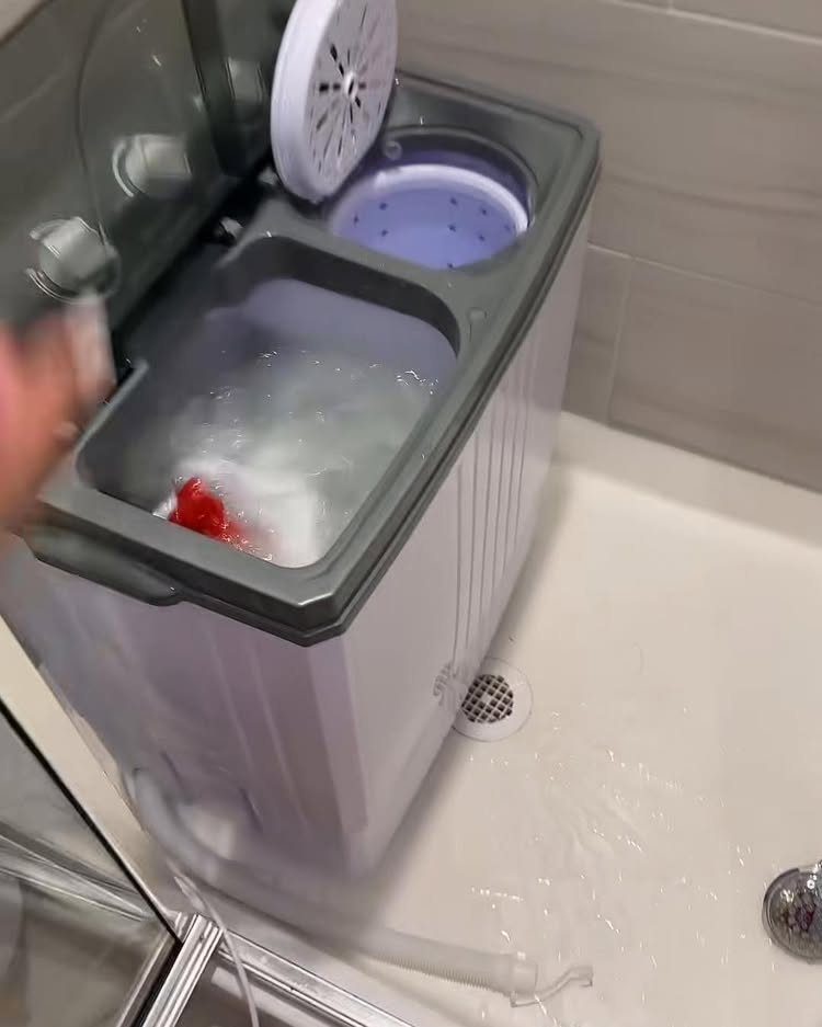 Portable twin-tub washing machine on a shower floor with soapy water inside.