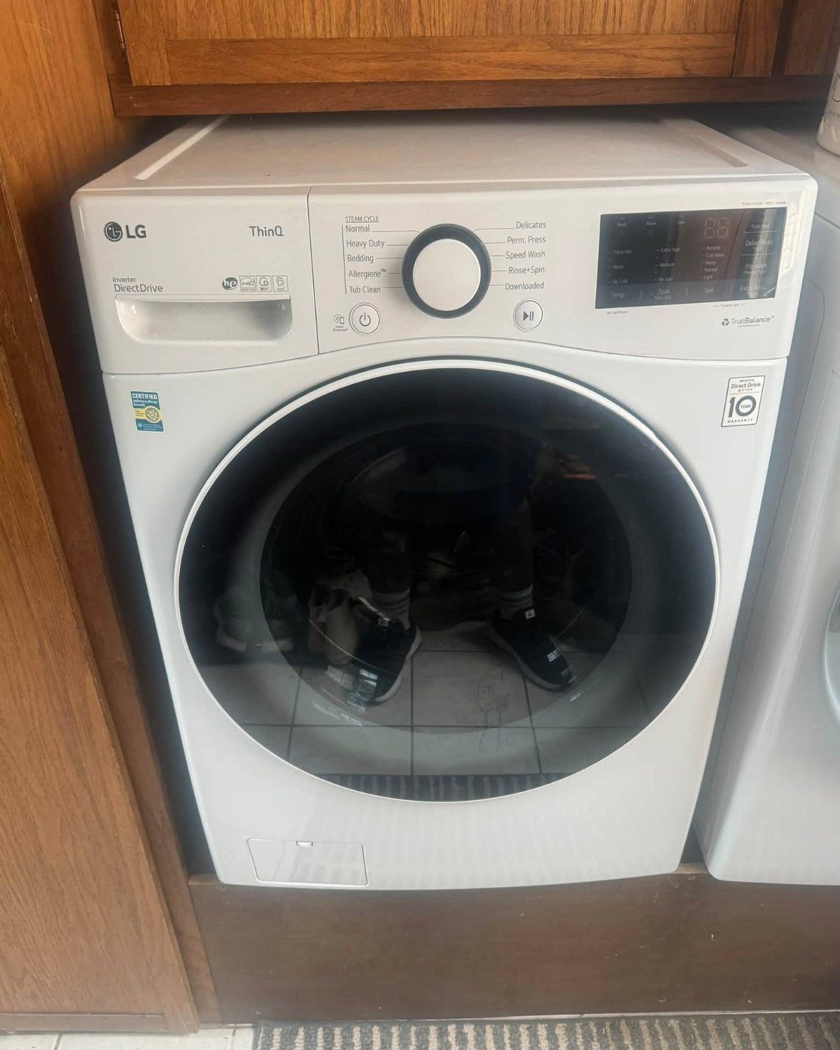 White LG front-load washing machine installed under wooden kitchen cabinets.