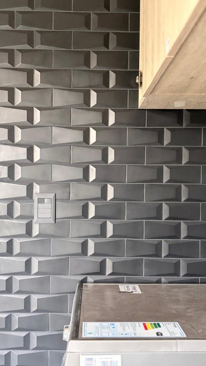 Grey 3D textured tile backsplash with a light switch and wooden cabinet.