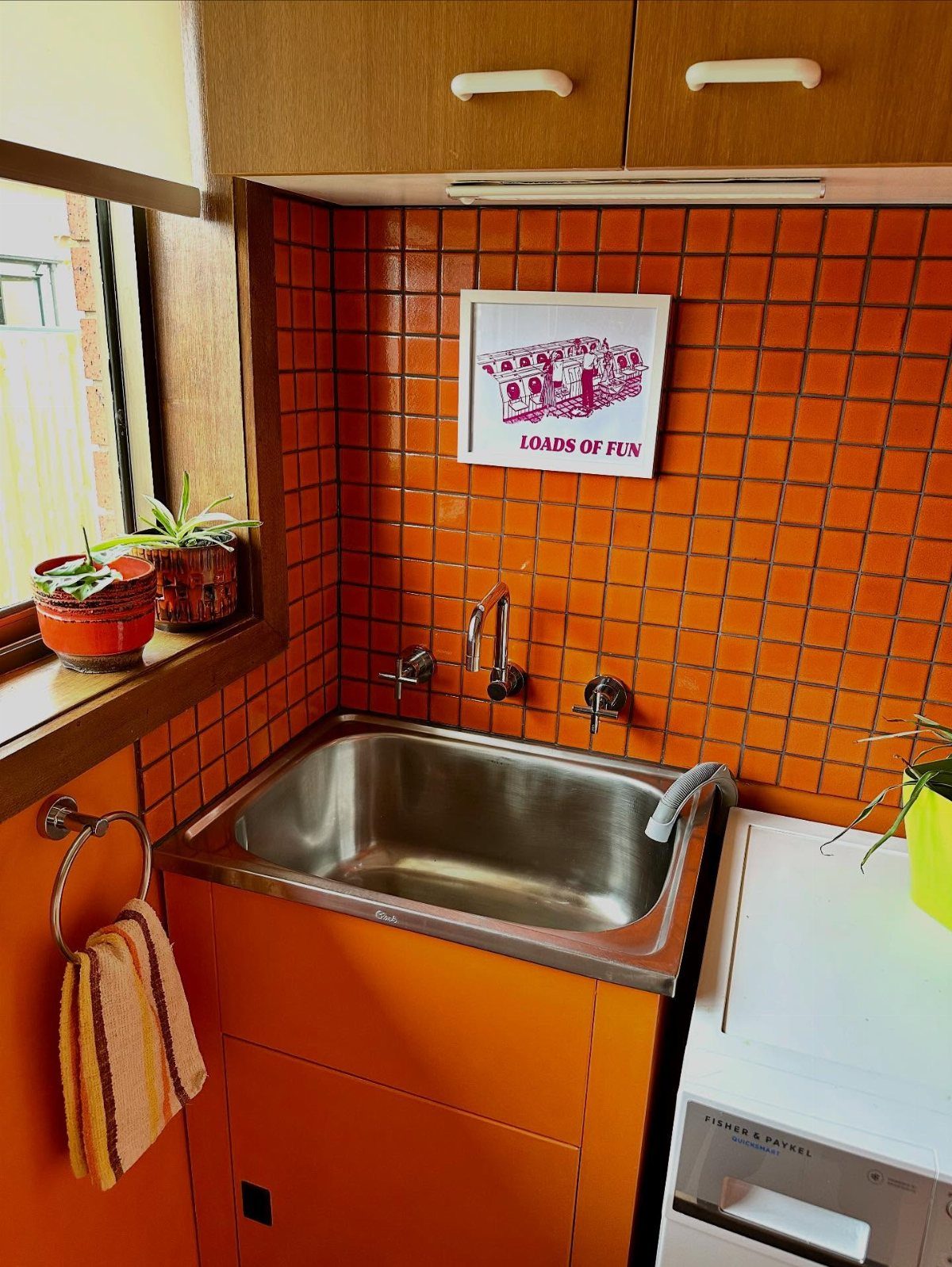 Orange square tile backsplash behind a stainless steel laundry sink and washing machine.
