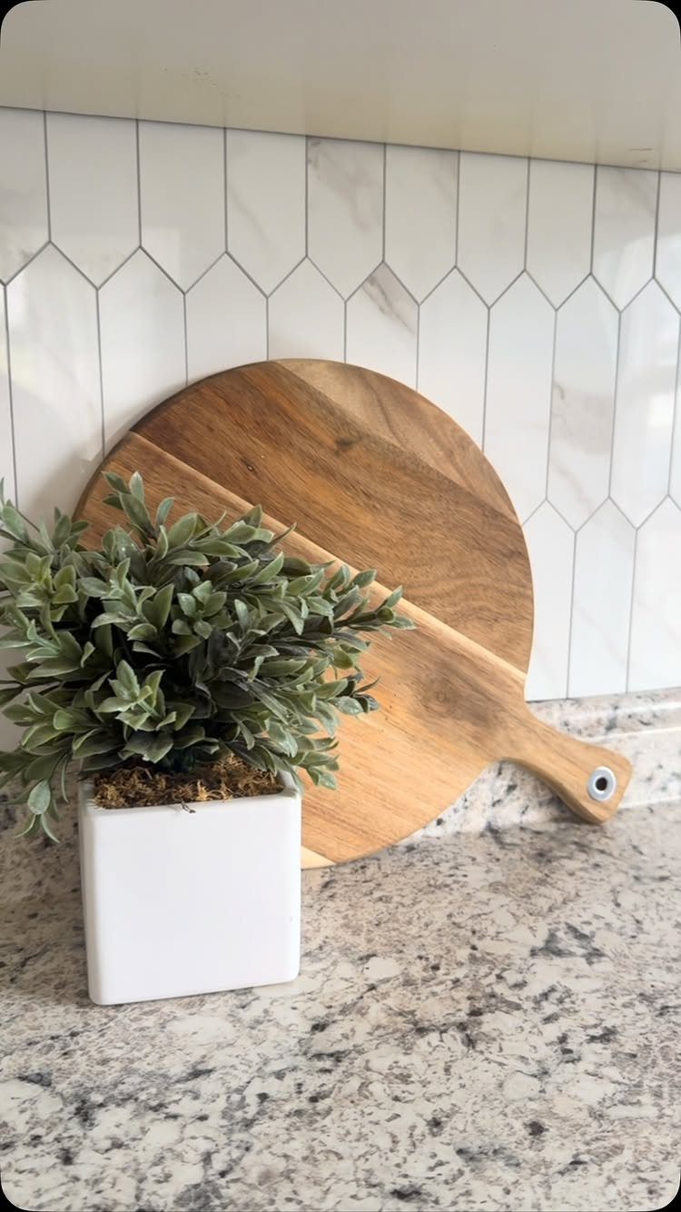 White marble hexagonal tile backsplash with a wooden cutting board and potted plant.