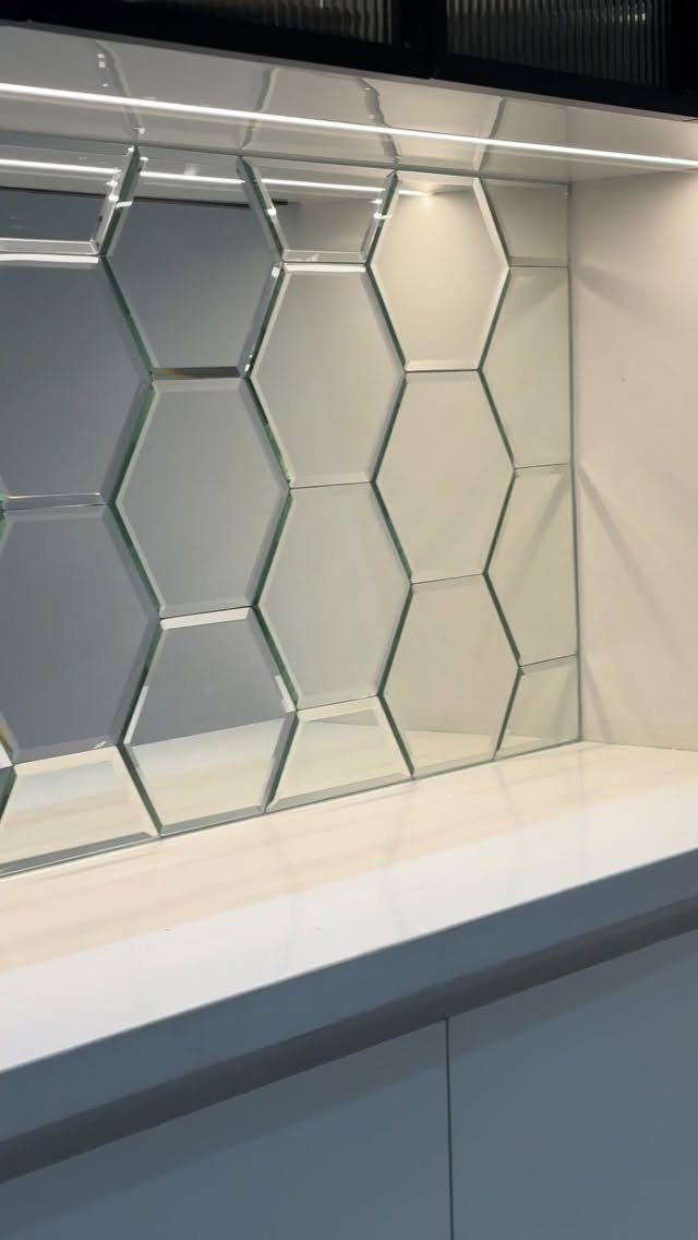 Mirrored hexagonal glass tiles as a backsplash above a white countertop.