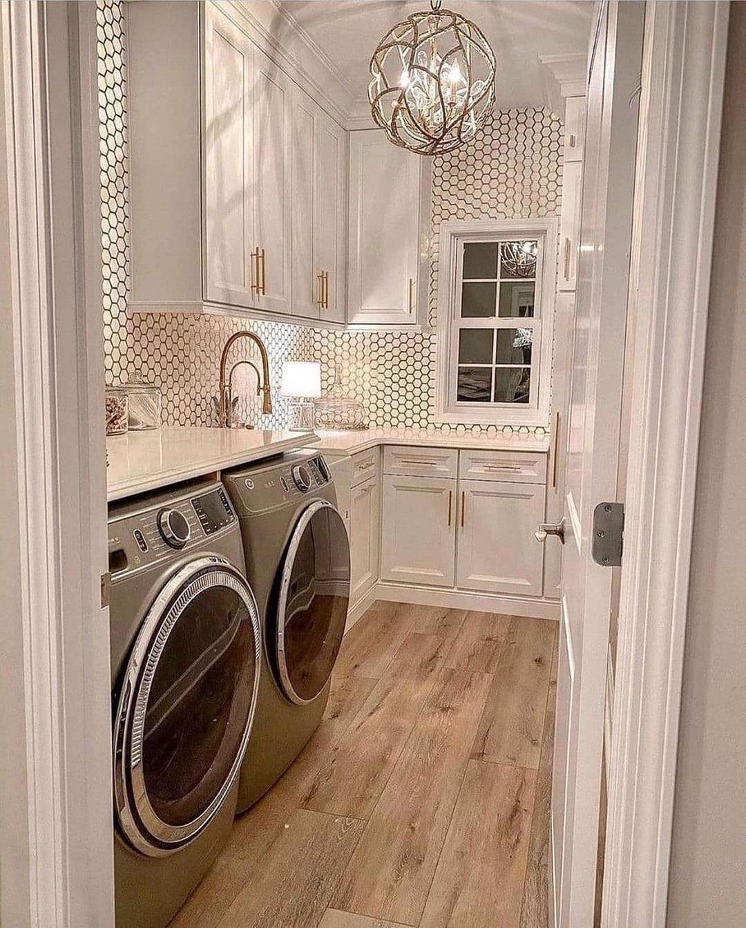 White honeycomb tile backsplash in a laundry room with white cabinets and gold accents.