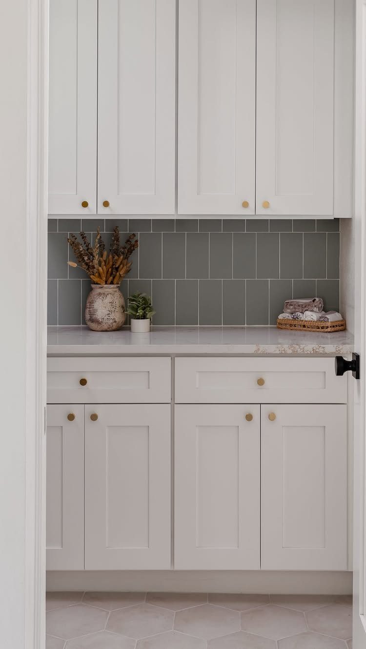 Grey subway tile backsplash between white upper and lower laundry room cabinets.