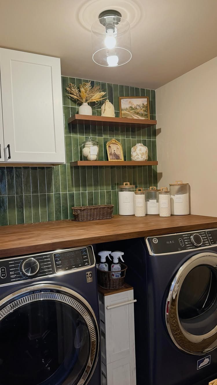 Green vertical tile backsplash behind a wooden counter and blue laundry machines.