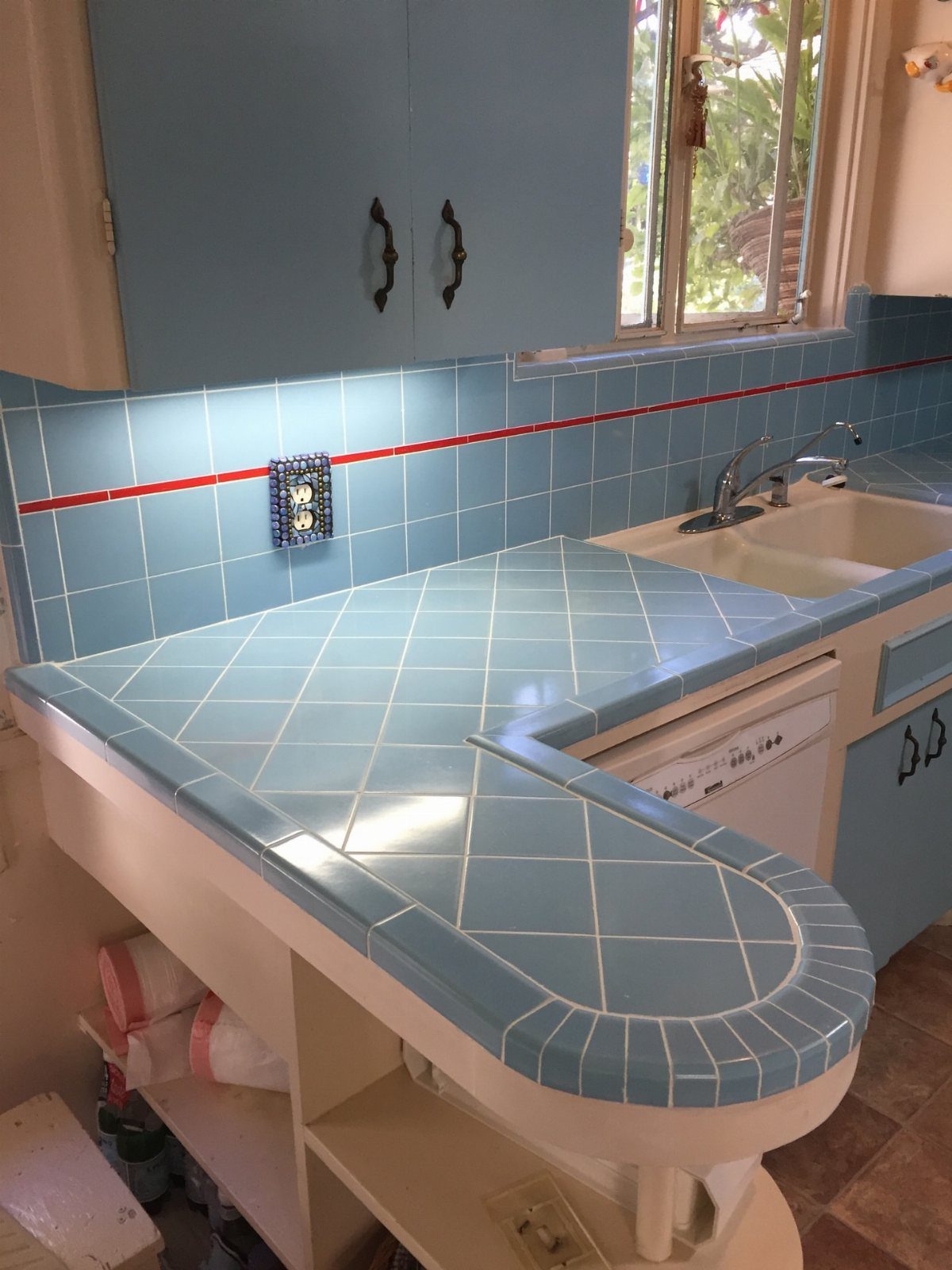Light blue square tiles on a countertop and backsplash with a red accent line.