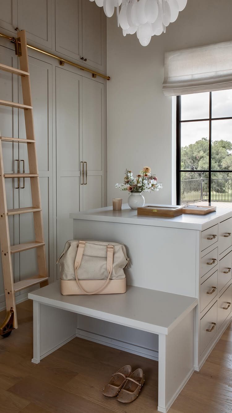 Closet island with drawers and a bench in a light grey walk-in closet.