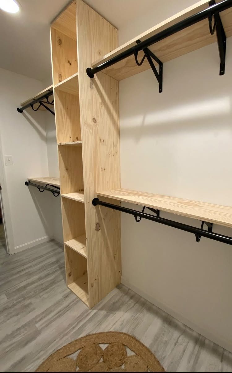 Wooden closet shelving and black hanging rods in a white walk-in closet.