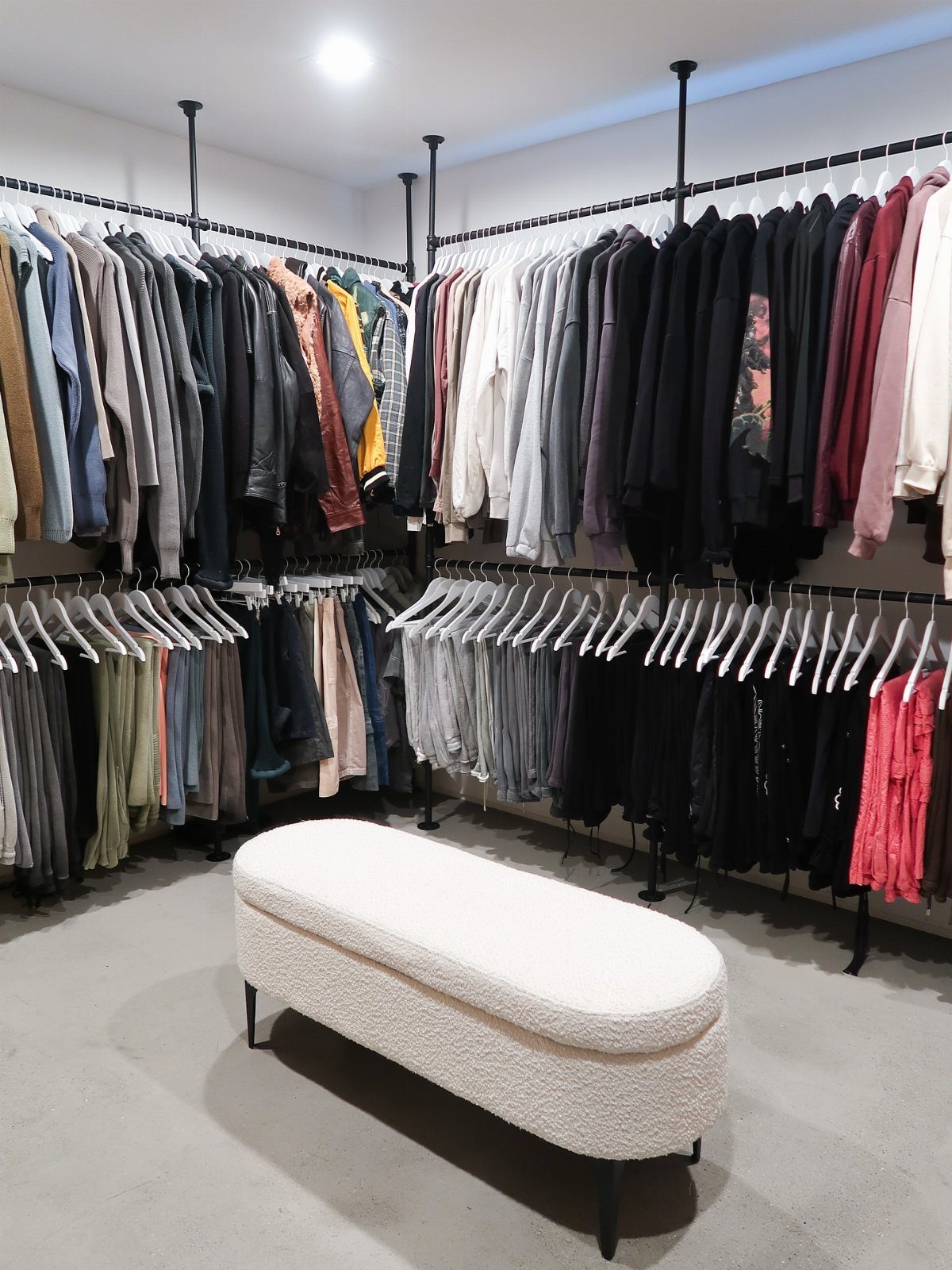 Walk-in closet with double-tier clothing racks and a white textured oval ottoman.