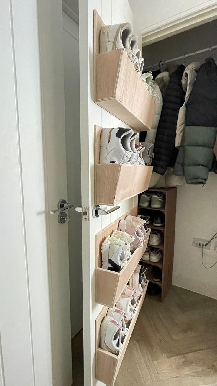 Wooden shoe shelves mounted on a white door holding several pairs of sneakers.