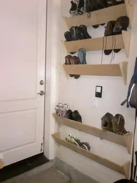 Wooden vertical shoe shelves mounted on a white wall next to a door.
