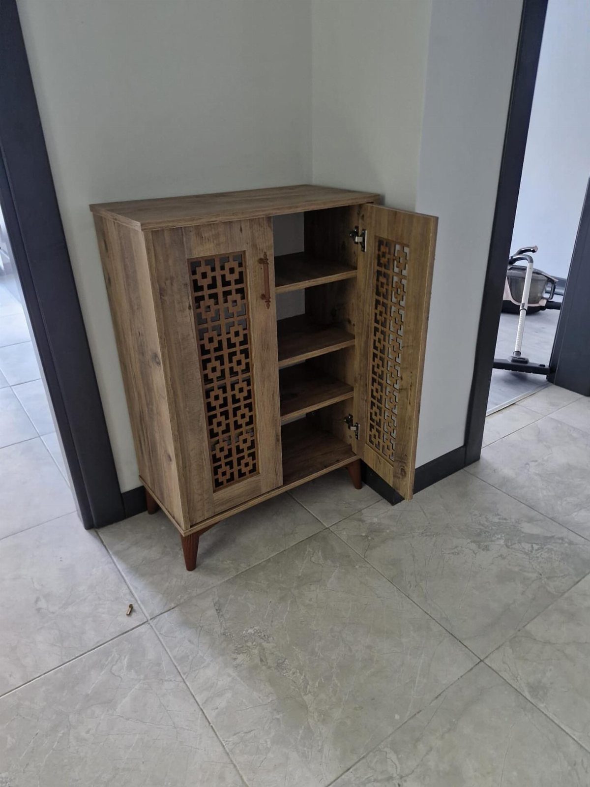 Wooden shoe cabinet with carved lattice doors and interior shelves on tiled floor