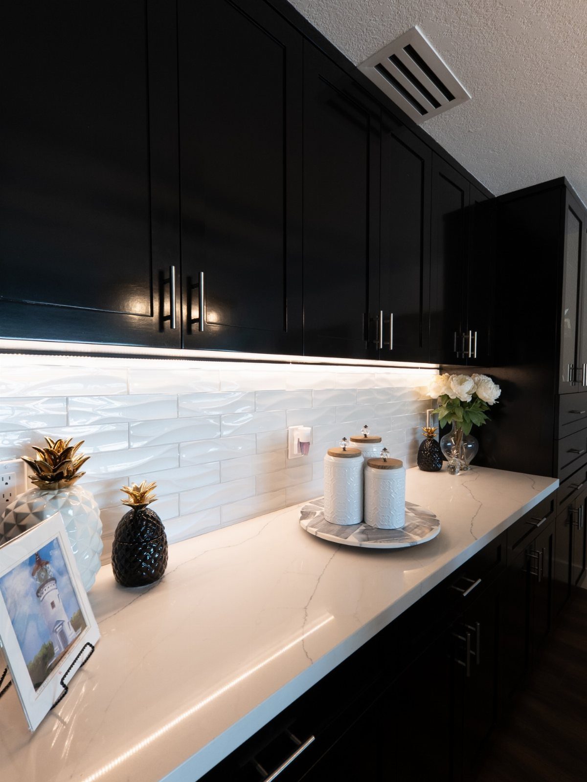 Black cabinets with silver hardware and white quartz countertops in a laundry room