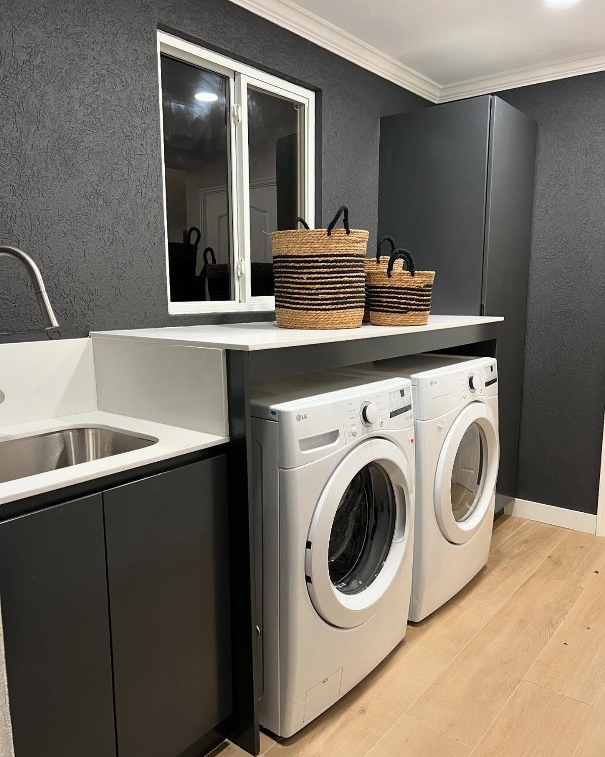 Black cabinets and white laundry machines in a modern laundry room with grey walls.