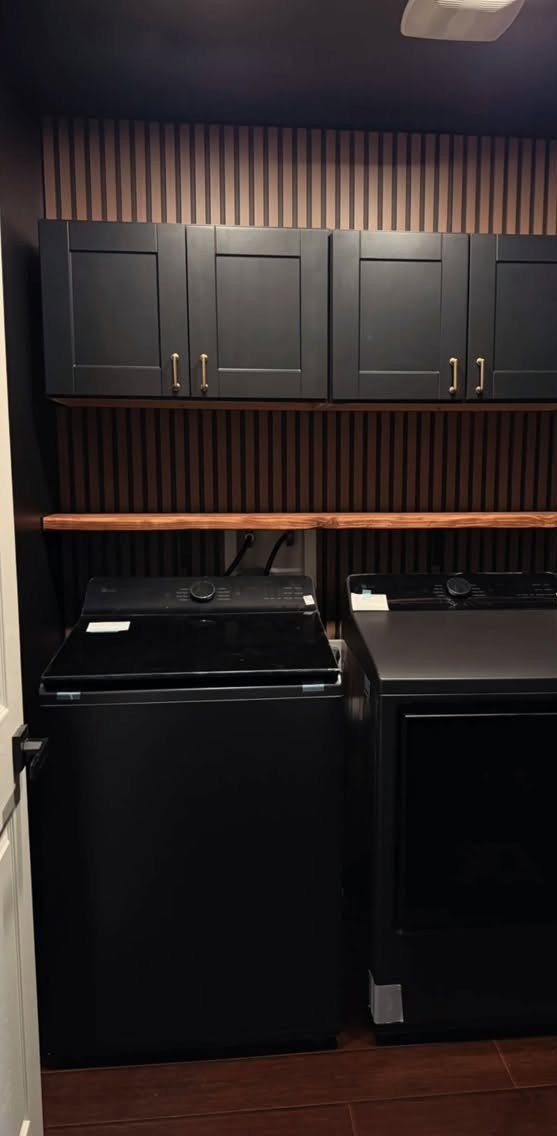 Black laundry cabinets and appliances against a dark brown vertical slat wall.
