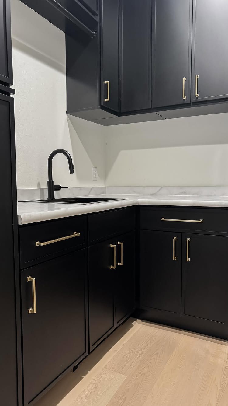 Black cabinets with gold hardware and white marble countertops in a modern room.