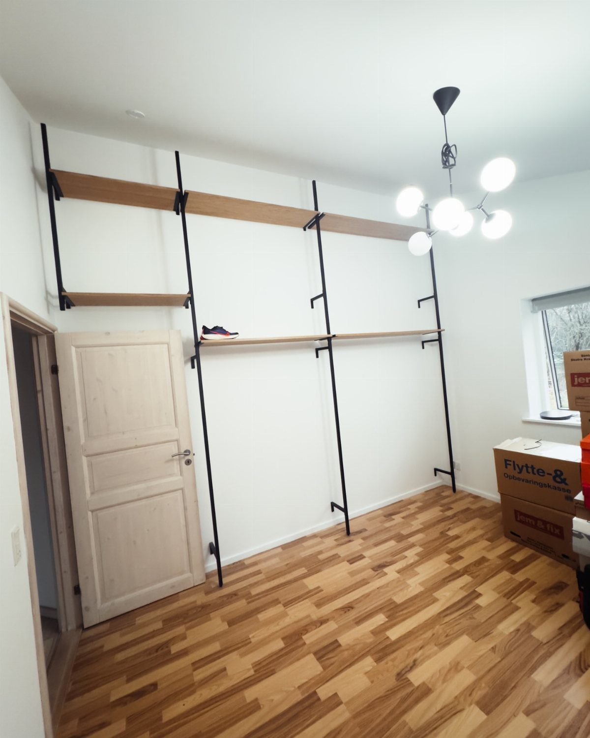 Wooden shelves on black metal rails installed against a white wall in a room.