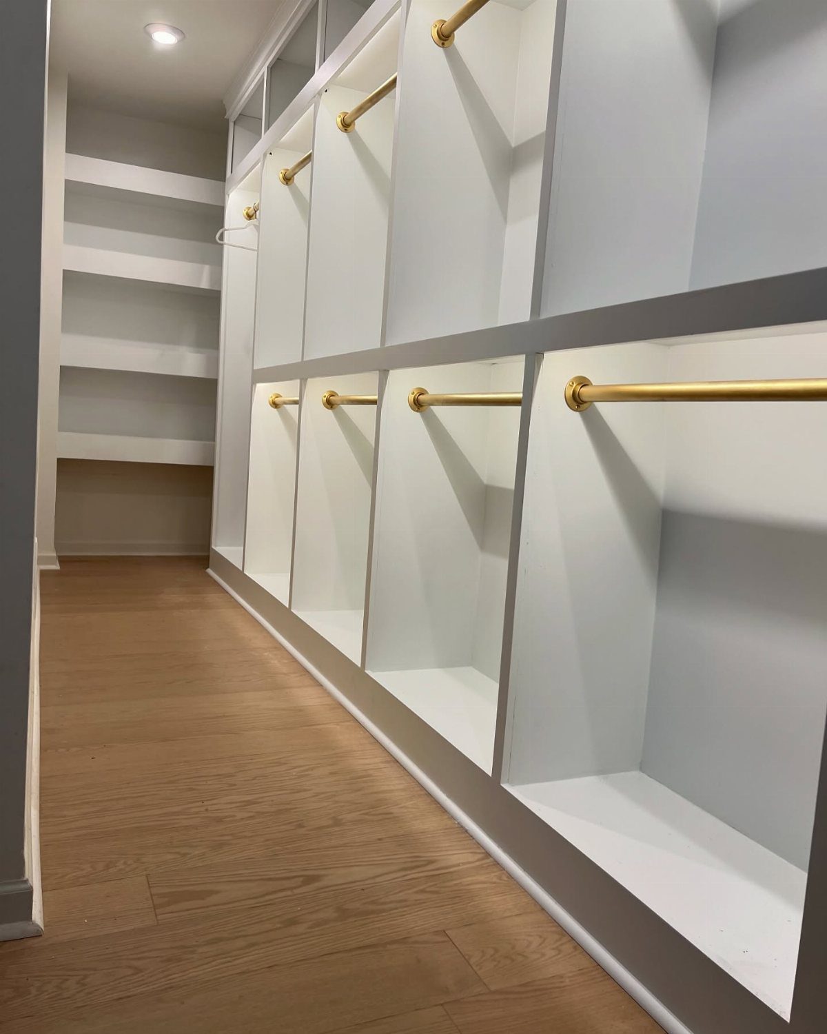 White built-in closet system with gold hanging rods and light wood flooring