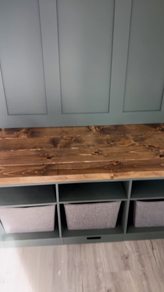 Built-in mudroom bench with wood top and grey bins in green cubbies.