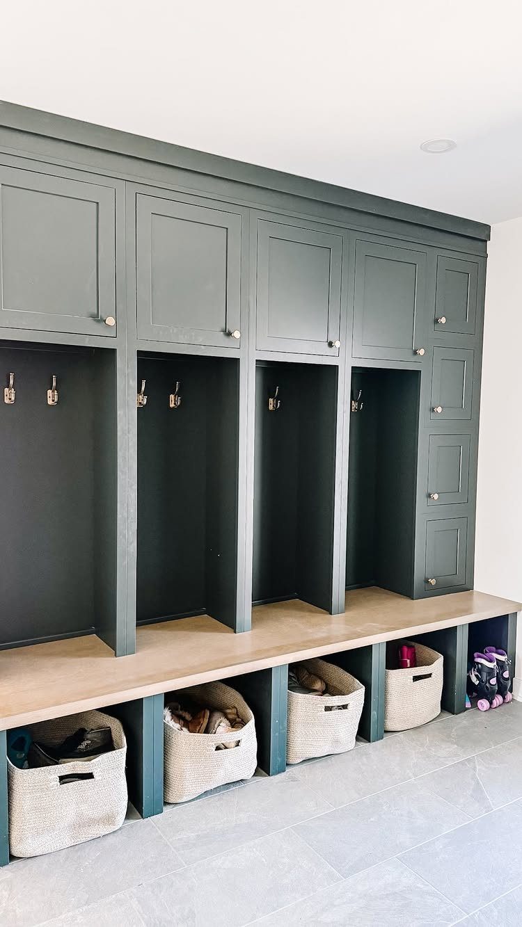 Grey built-in mudroom unit with a wooden bench, hooks, and woven storage baskets.