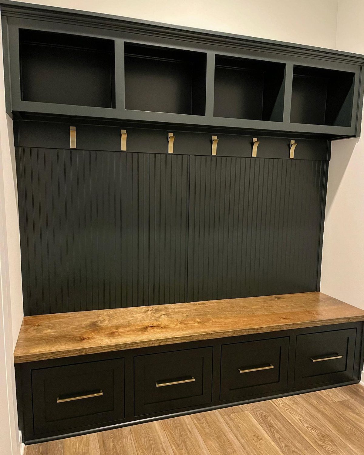 Black painted mudroom bench with wooden top, drawers, hooks, and overhead cubbies.