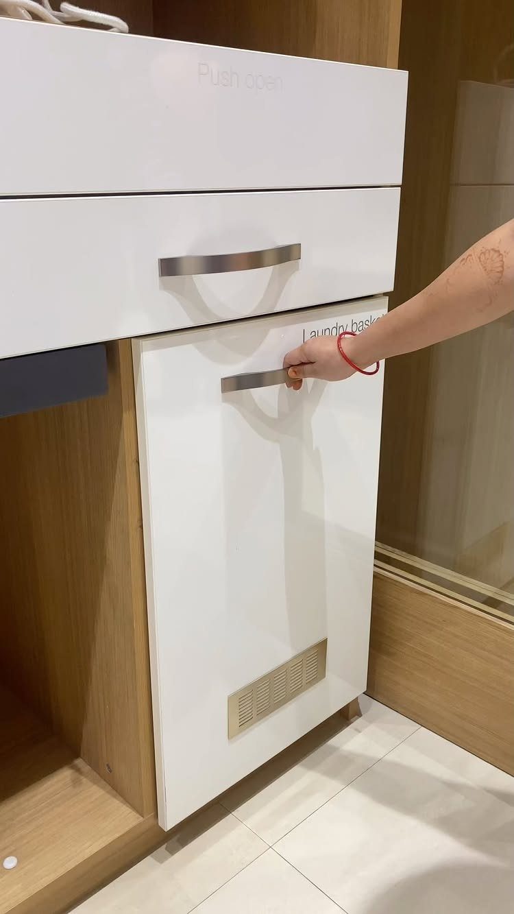 White pull-out laundry hamper drawer being opened in a light wood cabinet.