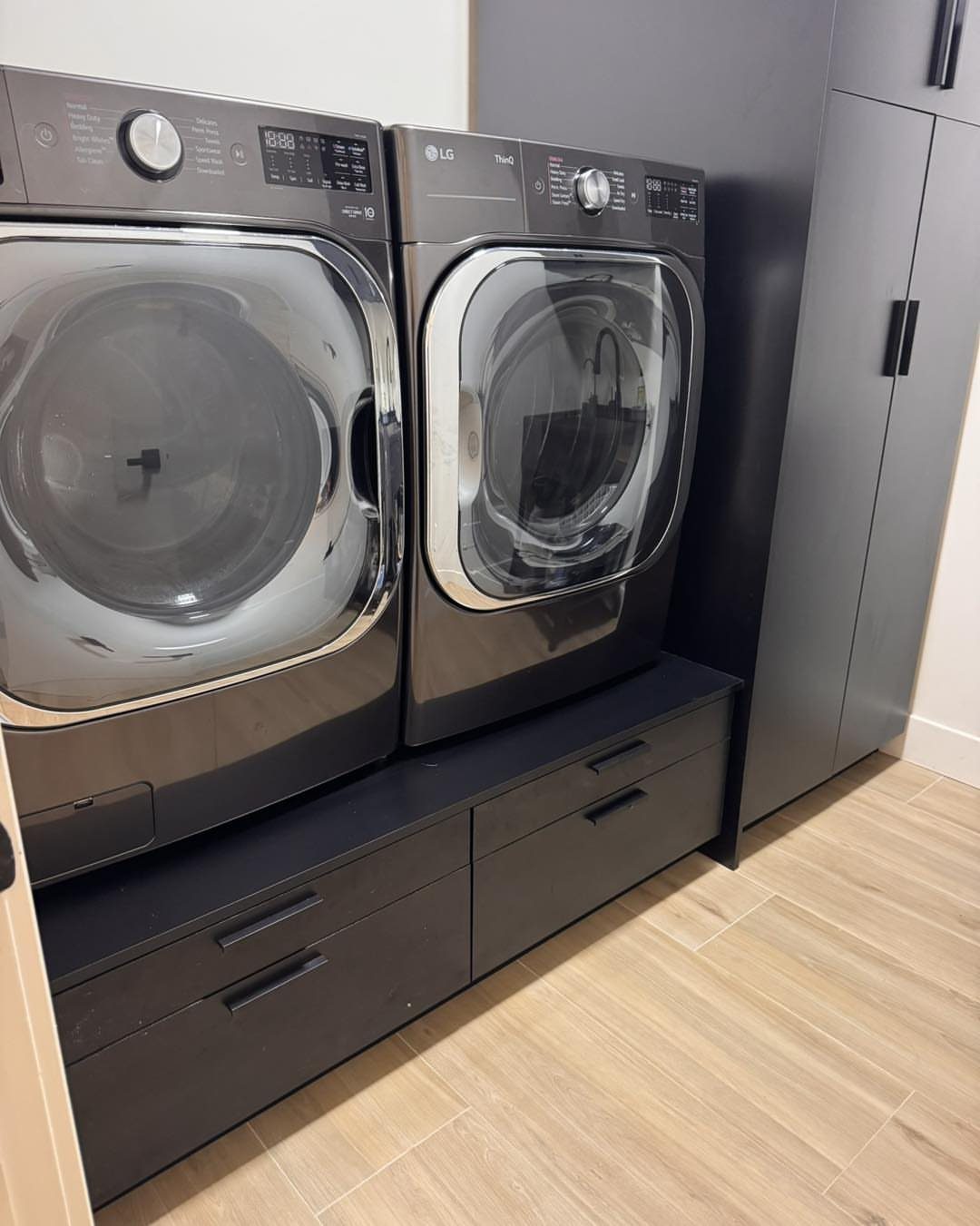Dark grey washer and dryer installed on a built-in cabinet with drawers.