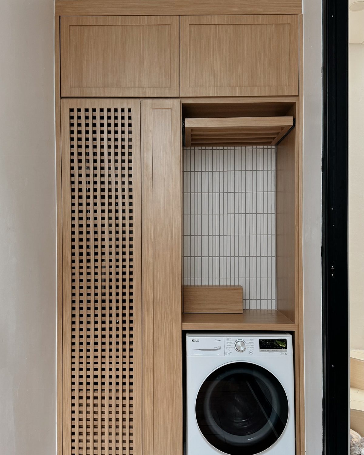 Light wood laundry cabinetry with upper cupboards and a white washing machine below.