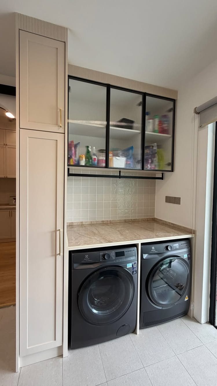 Black washer and dryer under a beige counter with glass cabinets above.