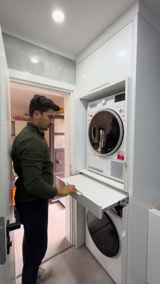 Stacked washer and dryer concealed within a white floor-to-ceiling cabinet with pull-out shelf.