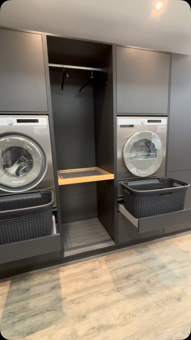 Modern utility room with dark grey cabinets, washing machines, and a hanging rail.
