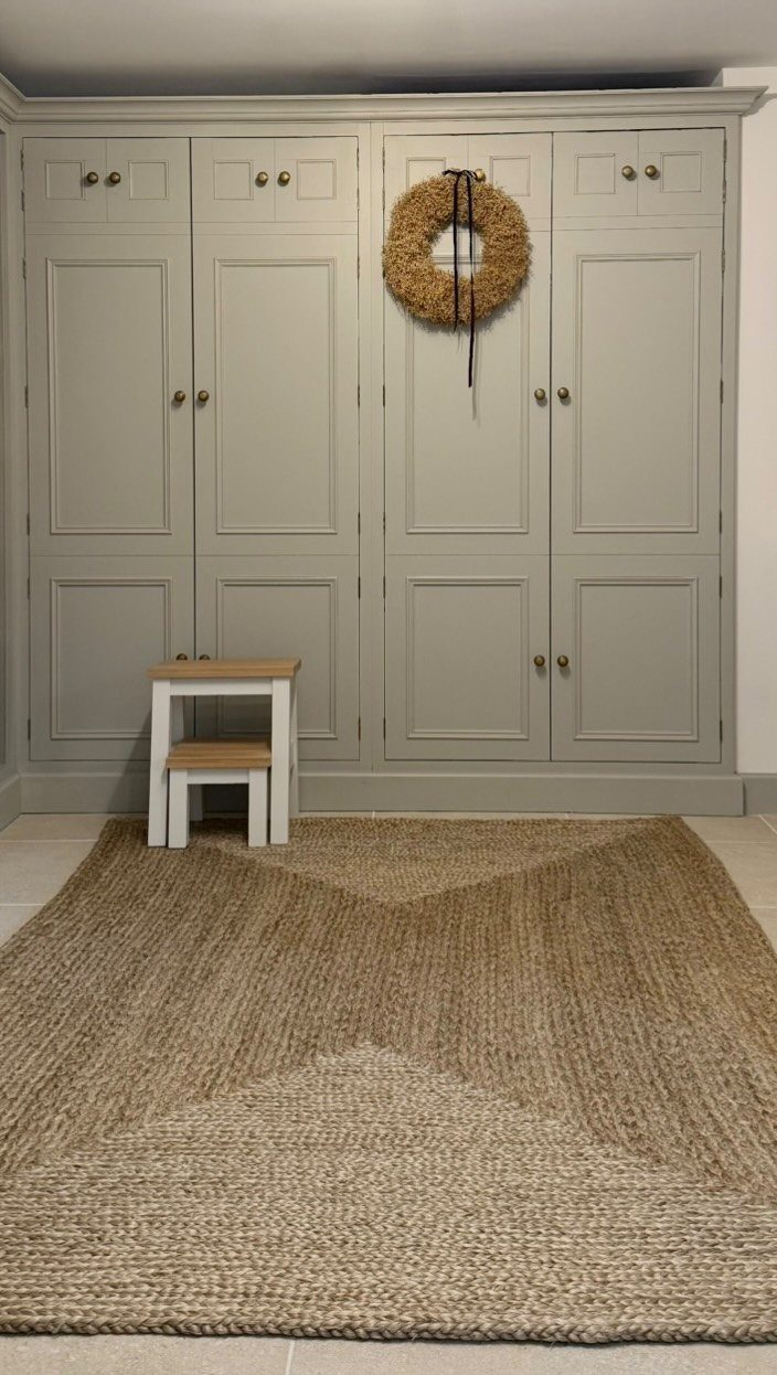 Grey built-in utility cabinets with a straw wreath and a jute rug.