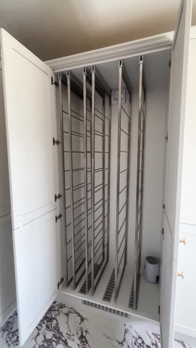 Foldable clothes airer installed inside a white built-in utility cupboard with marble flooring.