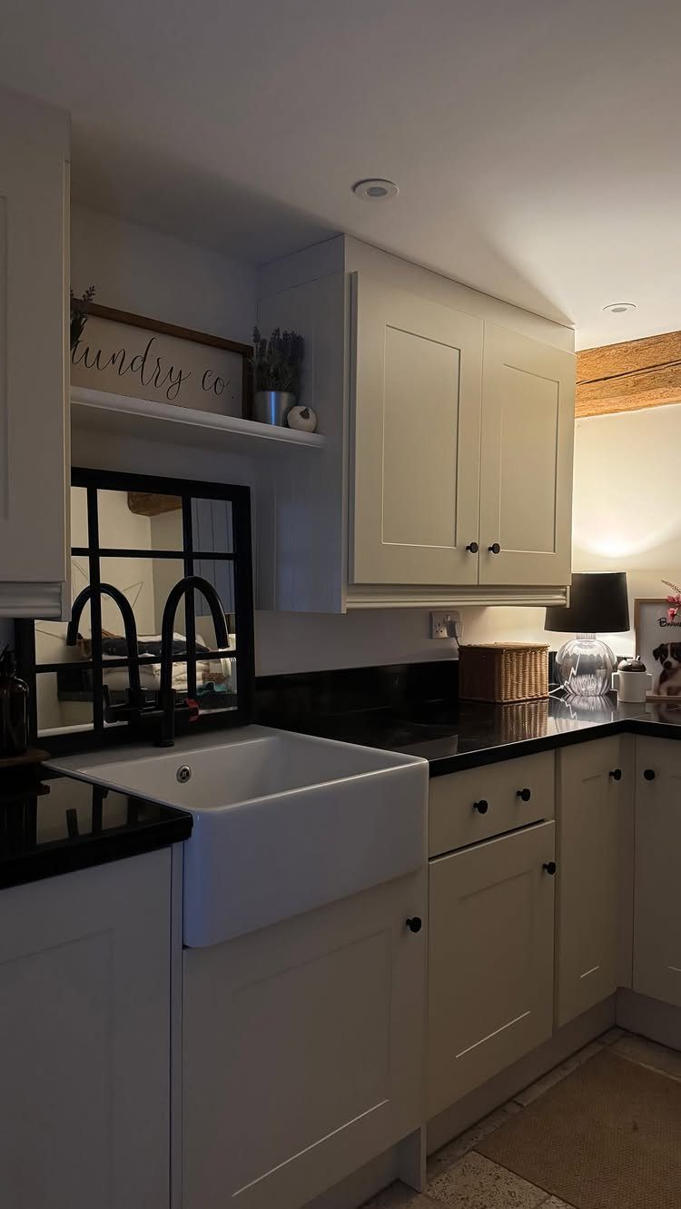 White utility room cabinets and farmhouse sink with contrasting black countertops and faucets.