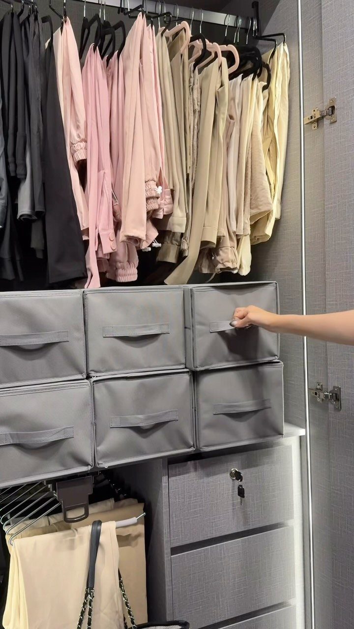 Closet with hanging clothes and grey fabric storage bins on a shelf.