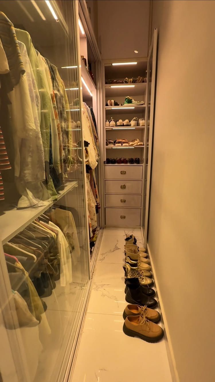 Narrow walk-in closet with white shelving and integrated LED strip lighting illuminating clothes.