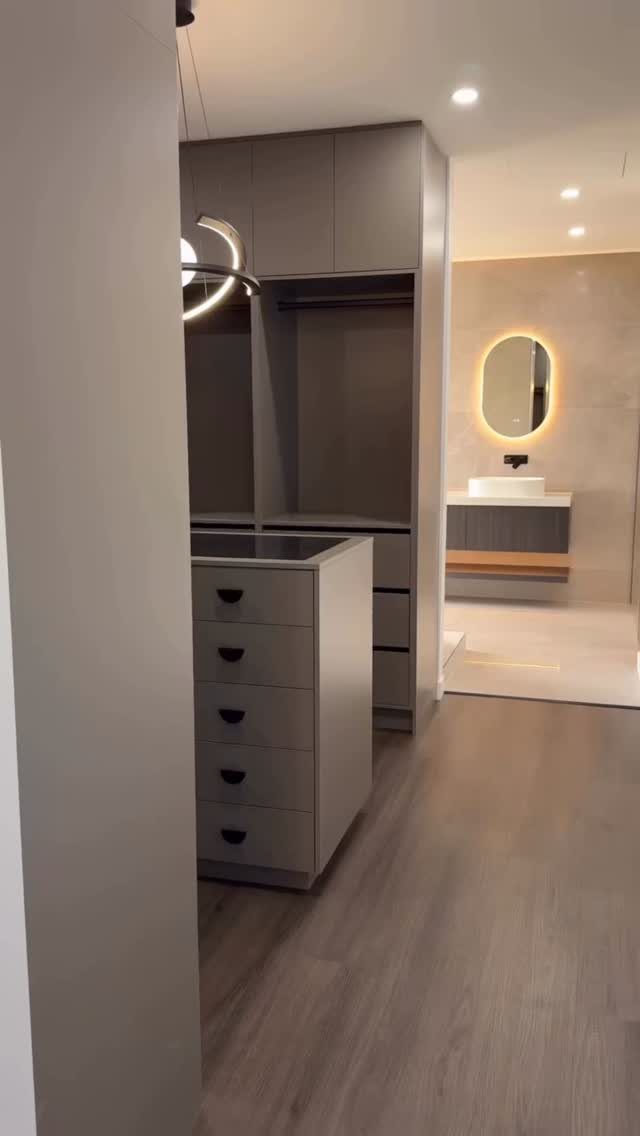 Grey built-in cabinets and drawers in a modern bathroom with a backlit mirror.